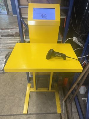 Yellow barcode scan station built by Garmet Ltd, with a touchscreen showing Standard Time's scan prompts and a handheld scanner on the table